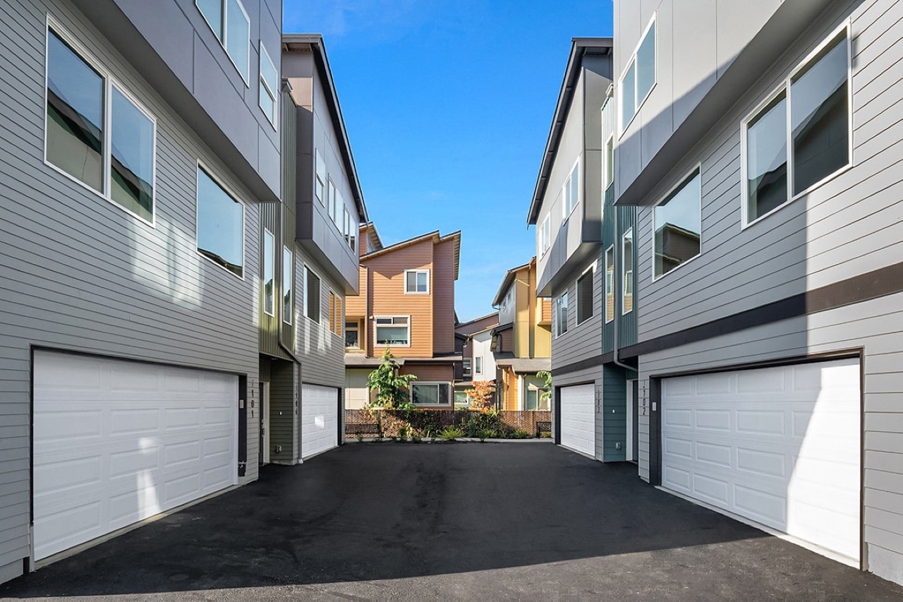 A driveway between two modern townhouses with grey siding and clean white garage doors under a clear blue sky.