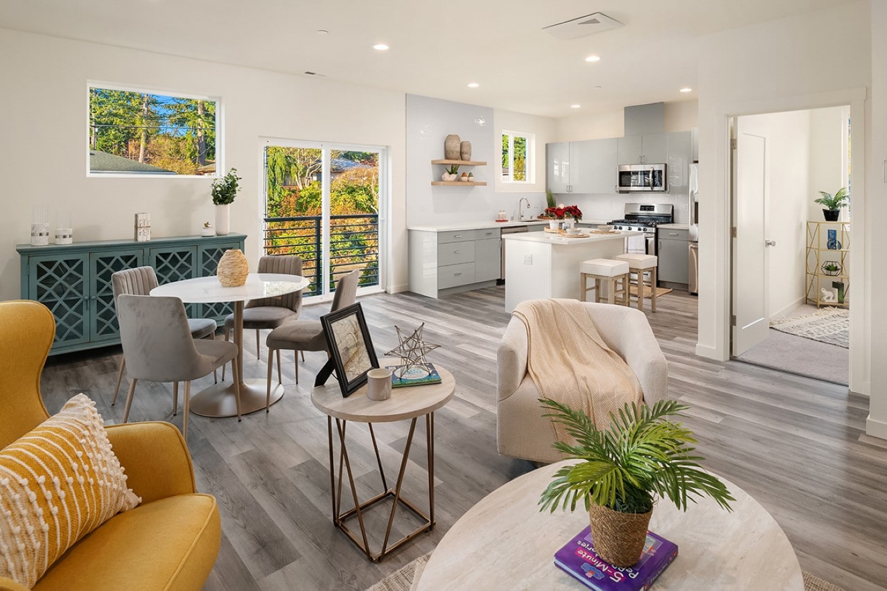 A stylish, open-concept living and dining room with colorful furniture that flows into a modern kitchen with grey cabinets.
