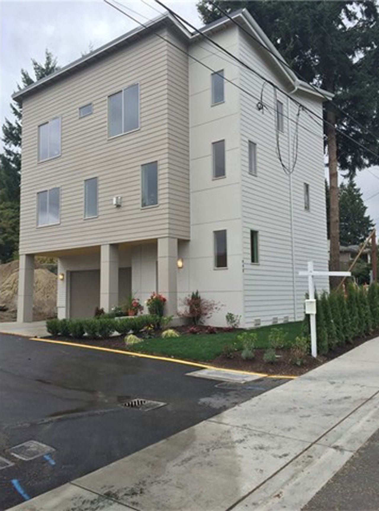  The exterior of a narrow, three-story modern home with light-colored siding, viewed from the street level.
