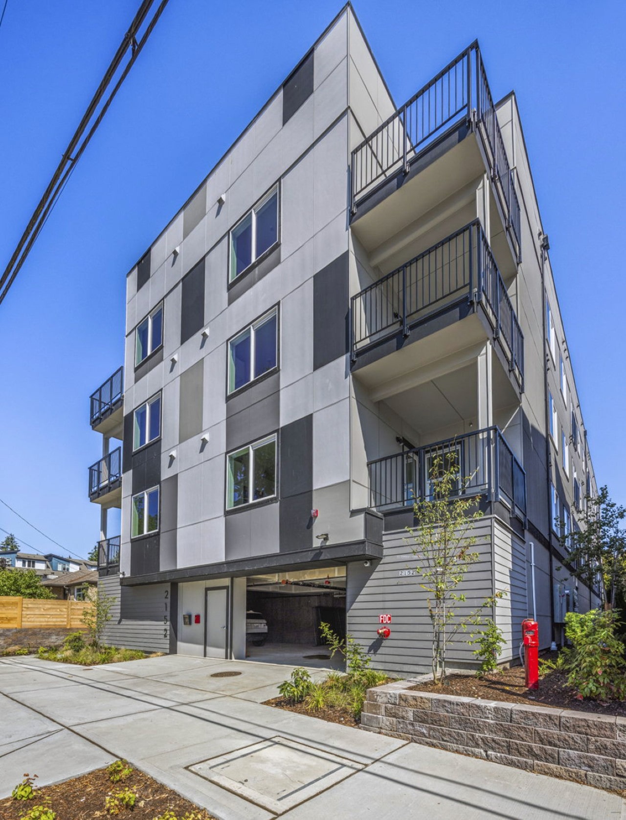 The exterior of a modern four-story apartment building with a gray and black checkered facade and multiple balconies.