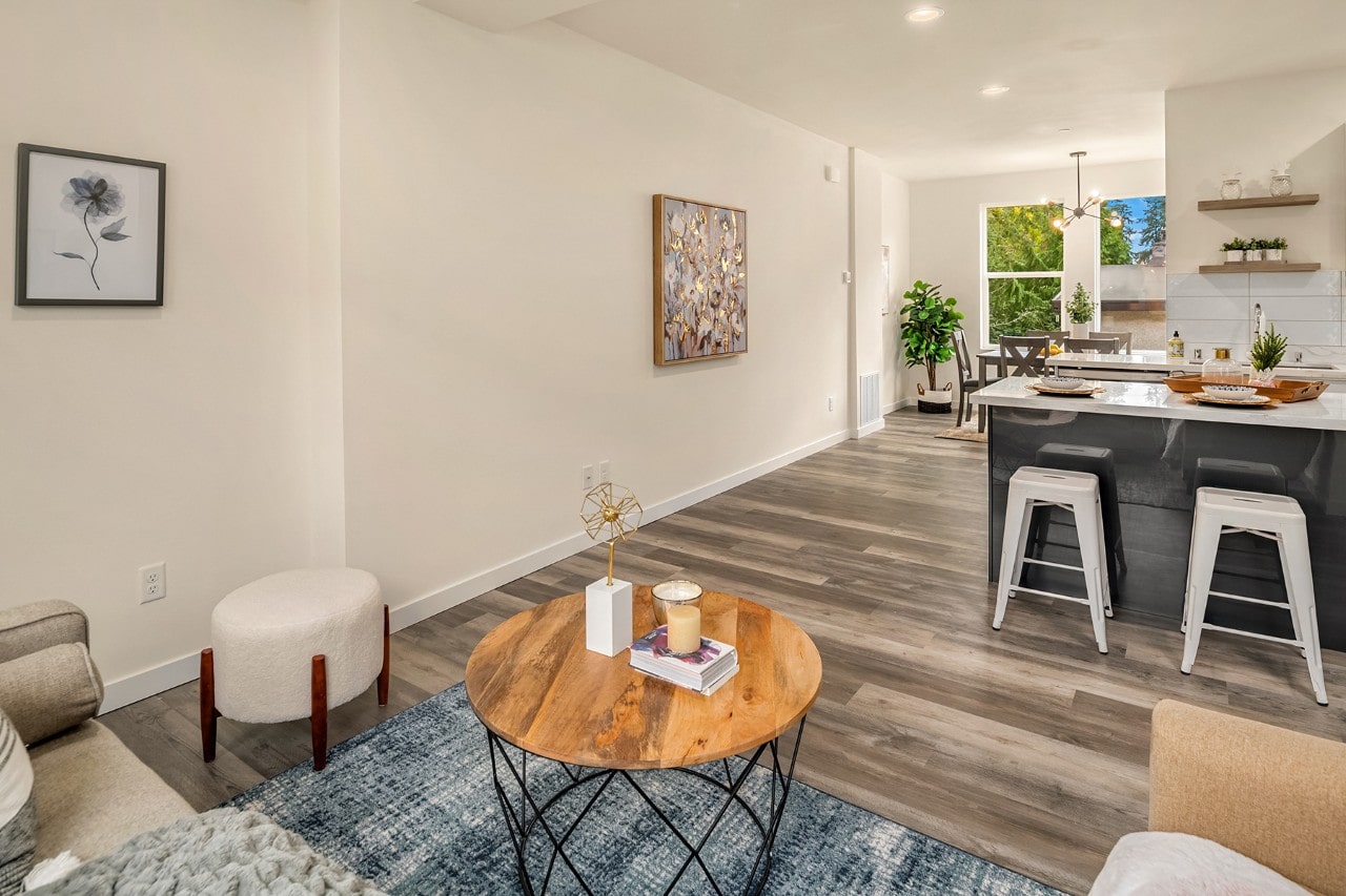 An open concept living space with wood-style flooring, a round wooden coffee table, and view into the kitchen with a dark island.