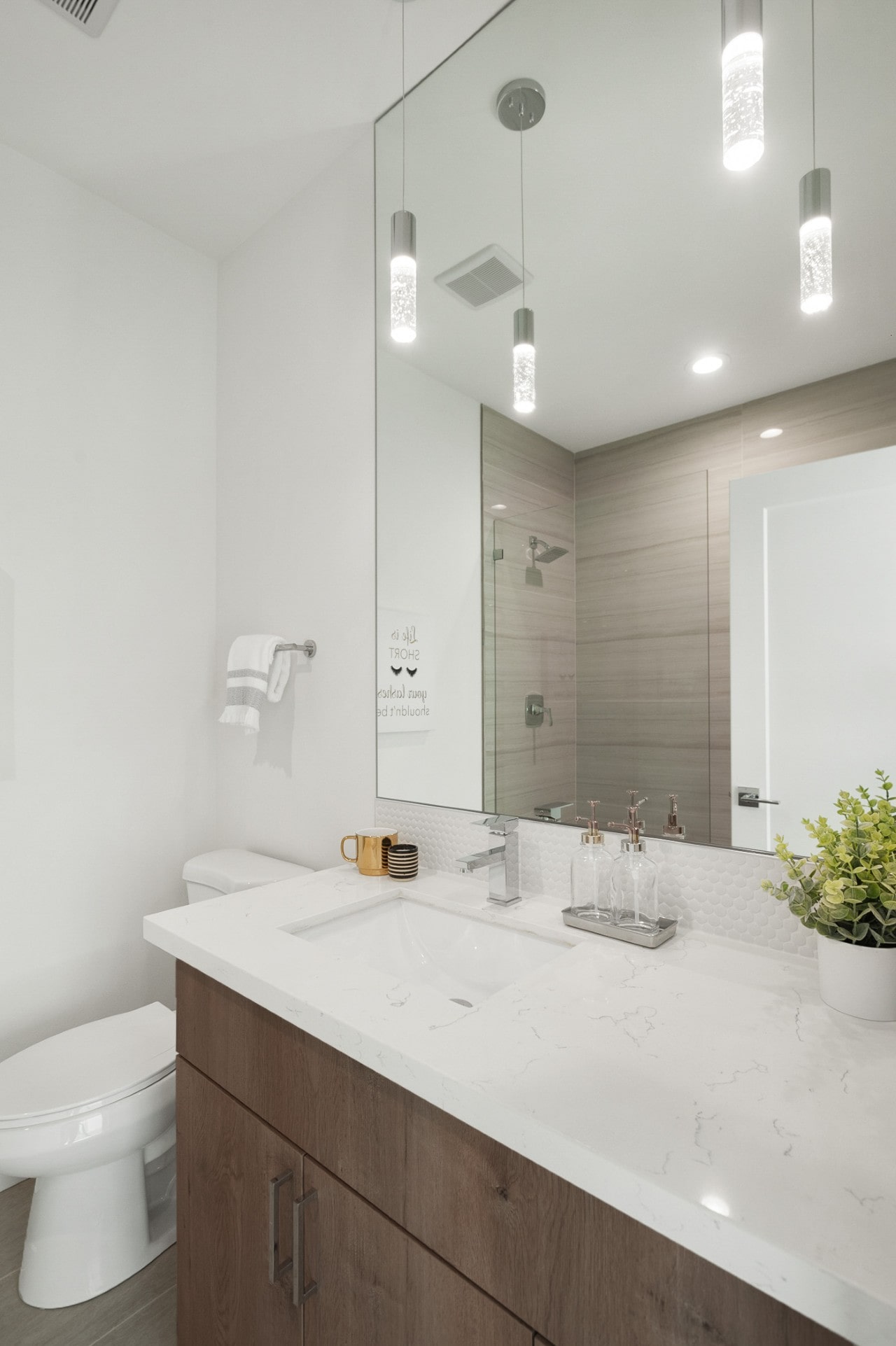 A modern bathroom with a white quartz countertop, wood-grain vanity, and elegant hanging pendant lights over the sink.