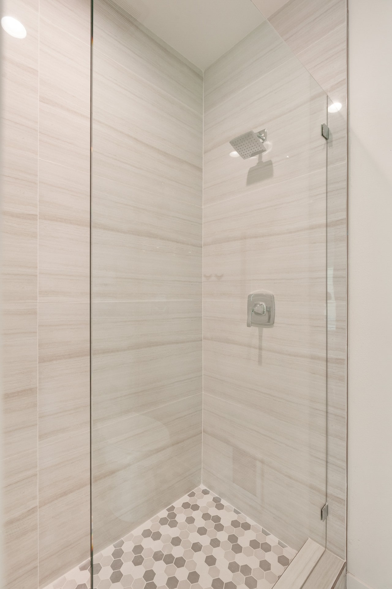 A close-up of a contemporary walk-in shower with a glass door, chrome rain shower head, and hexagonal floor tiles.