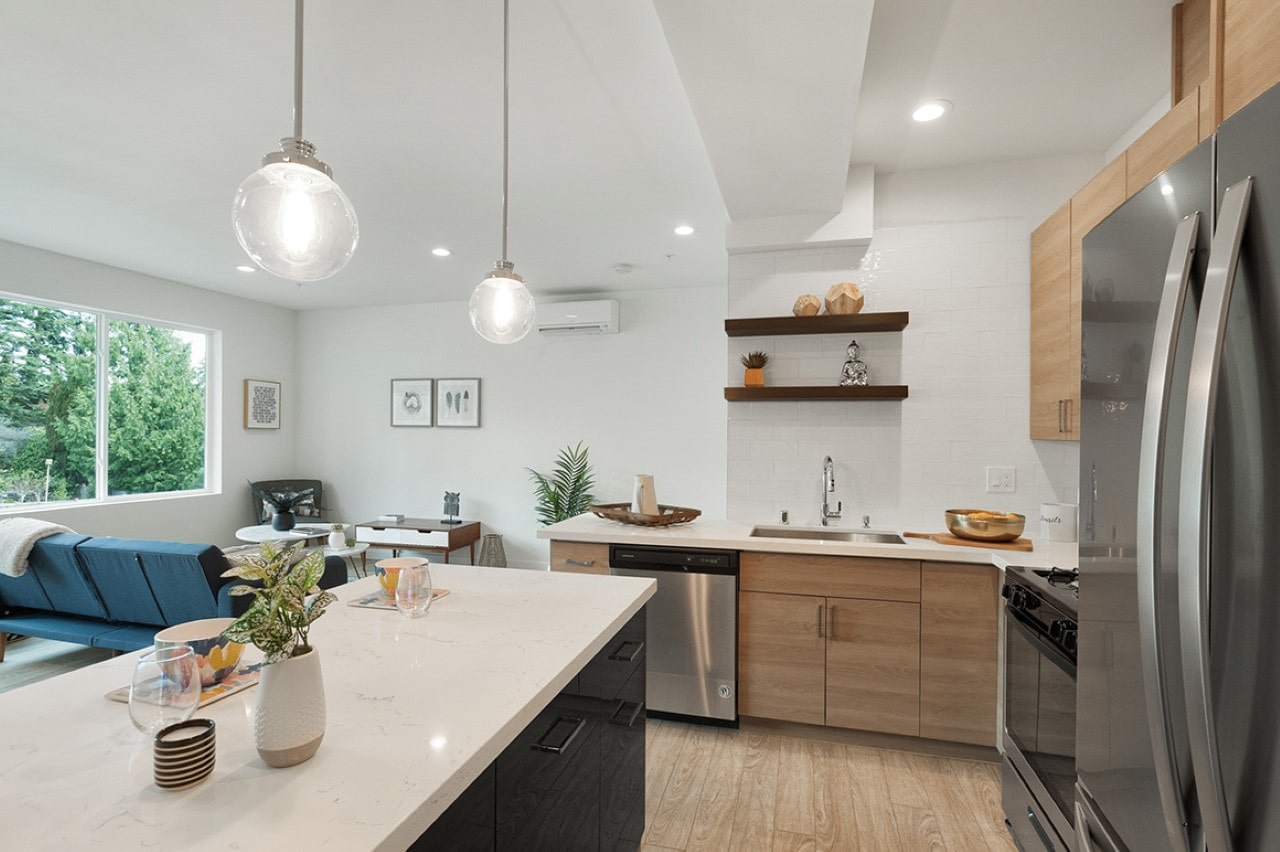 An open concept kitchen and living room featuring a large island with a white countertop and views of the neighborhood through large windows.