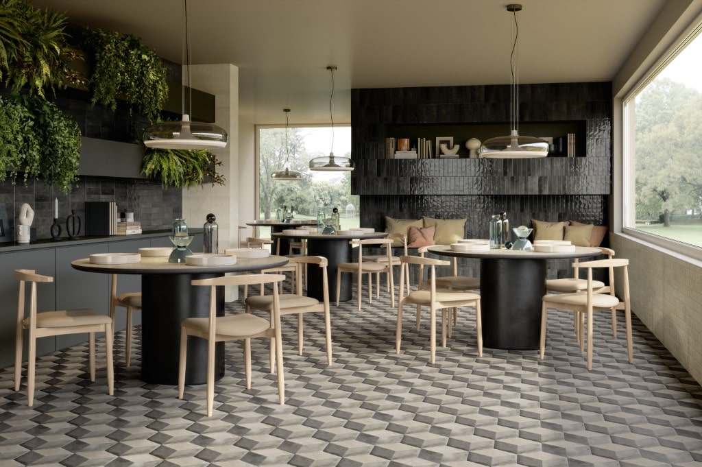A chic restaurant dining area with round tables, light wood chairs, hanging plants, and a striking grey geometric-patterned tile floor.