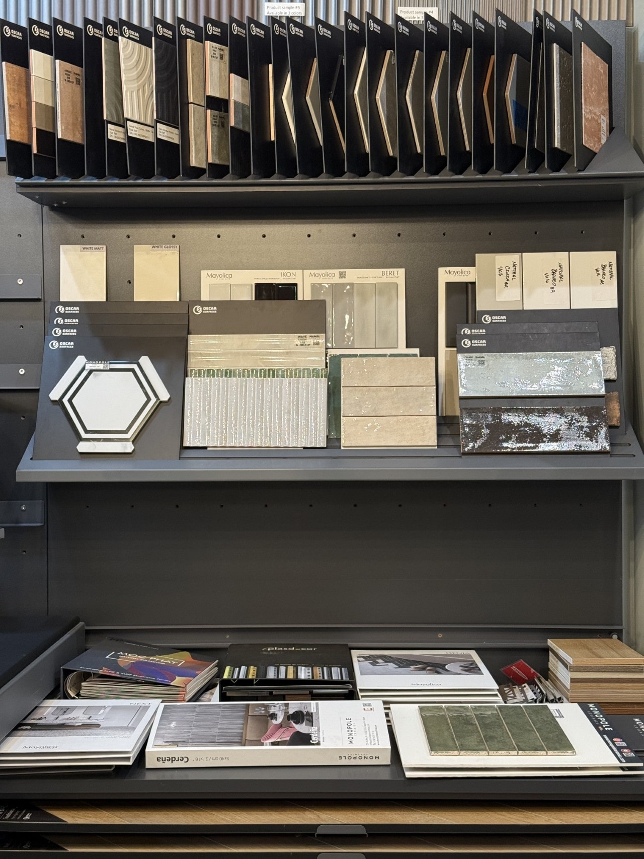 A showroom display shelf neatly organized with various tile samples, including hexagonal and rectangular tiles, alongside interior design catalogs.