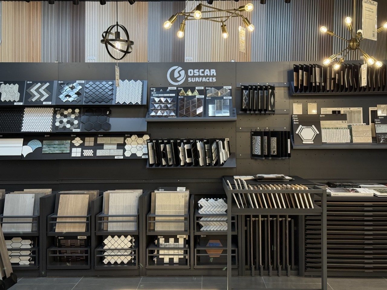 The Oscar Surfaces showroom featuring a large display wall with a wide variety of tile samples, illuminated by contemporary light fixtures.