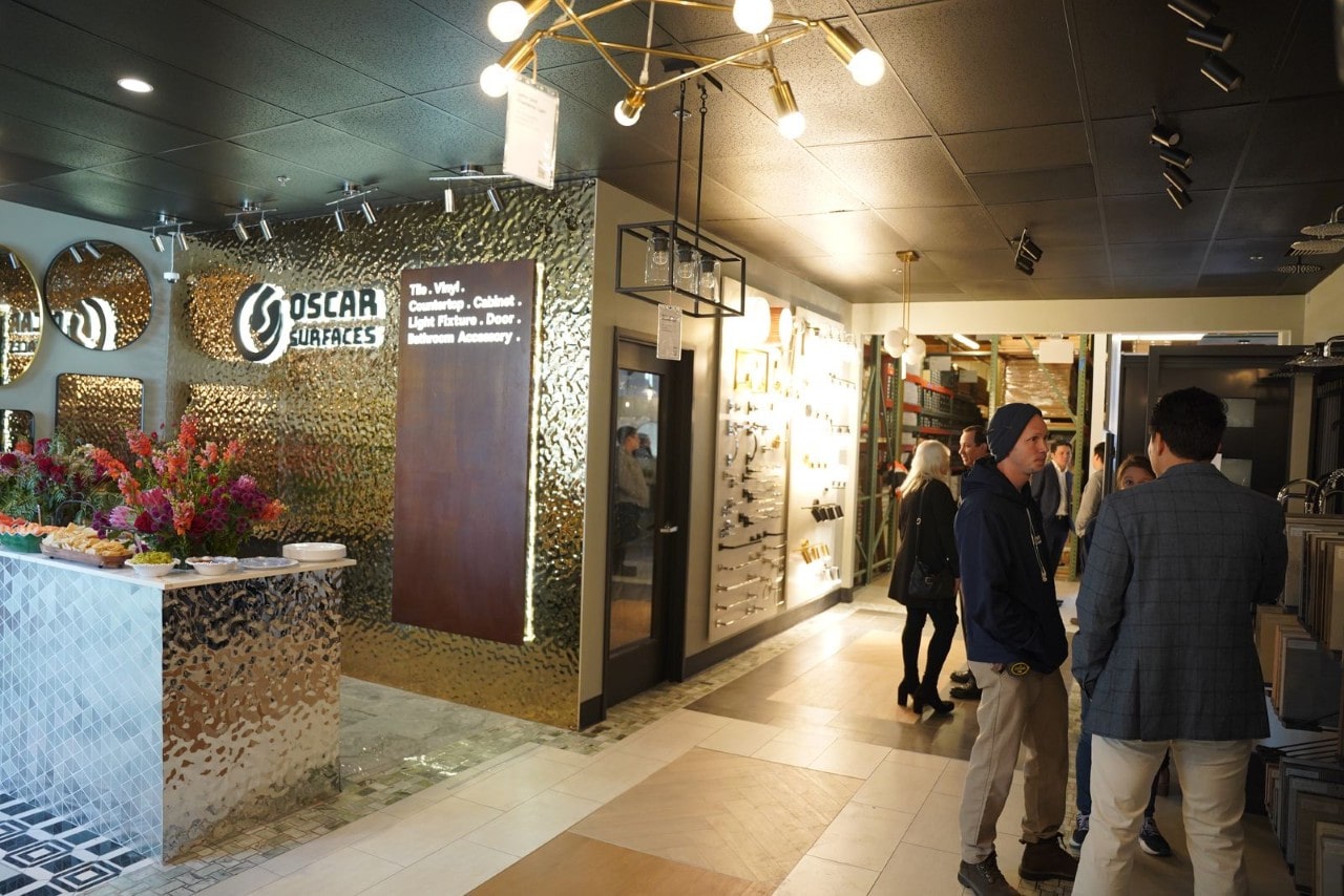 The interior of the Oscar Surfaces showroom with customers browsing displays, featuring a hammered gold accent wall and a modern sputnik chandelier.