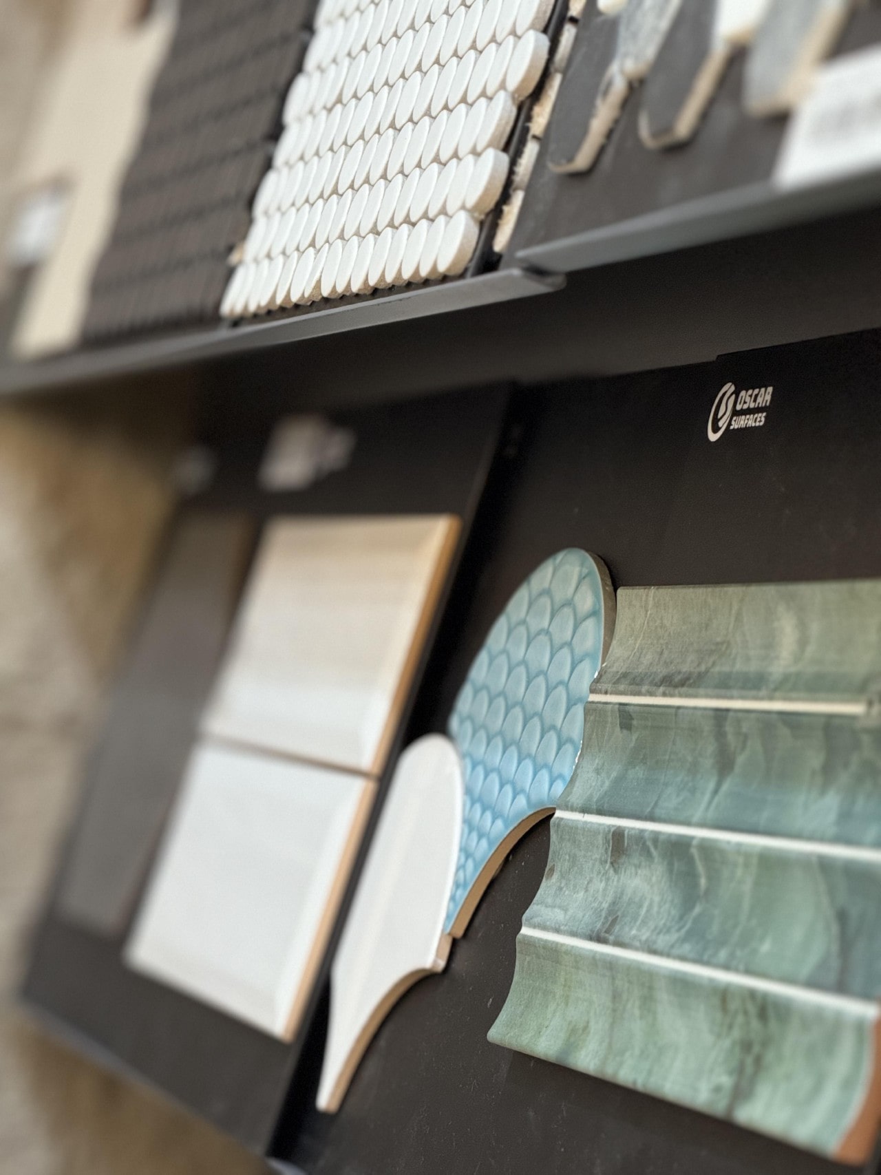 A close-up shot of decorative tile samples on a display rack, with blue fish-scale and green glazed tiles in sharp focus.