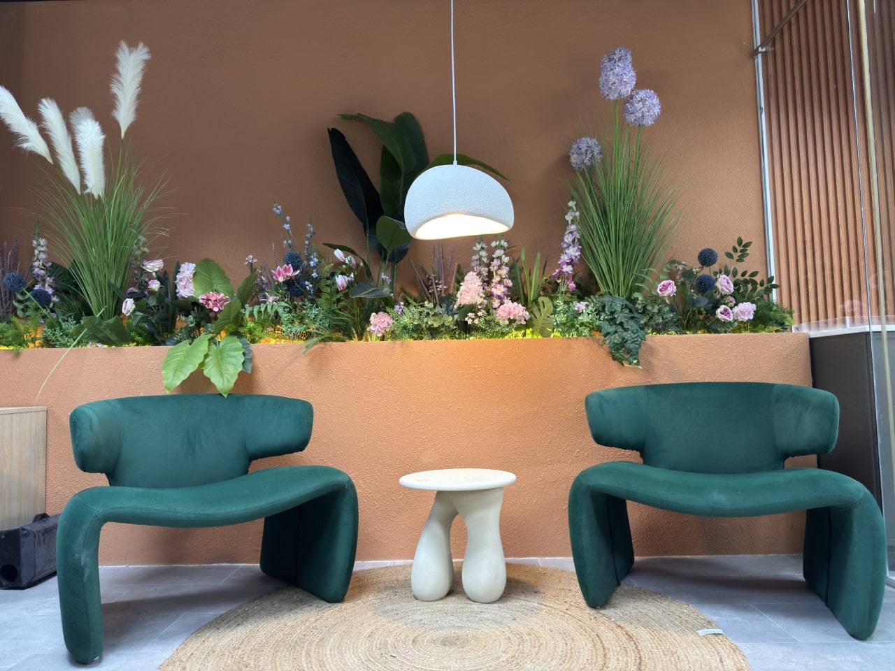 A modern waiting area with two sculptural green velvet armchairs and a unique white side table on a round jute rug.