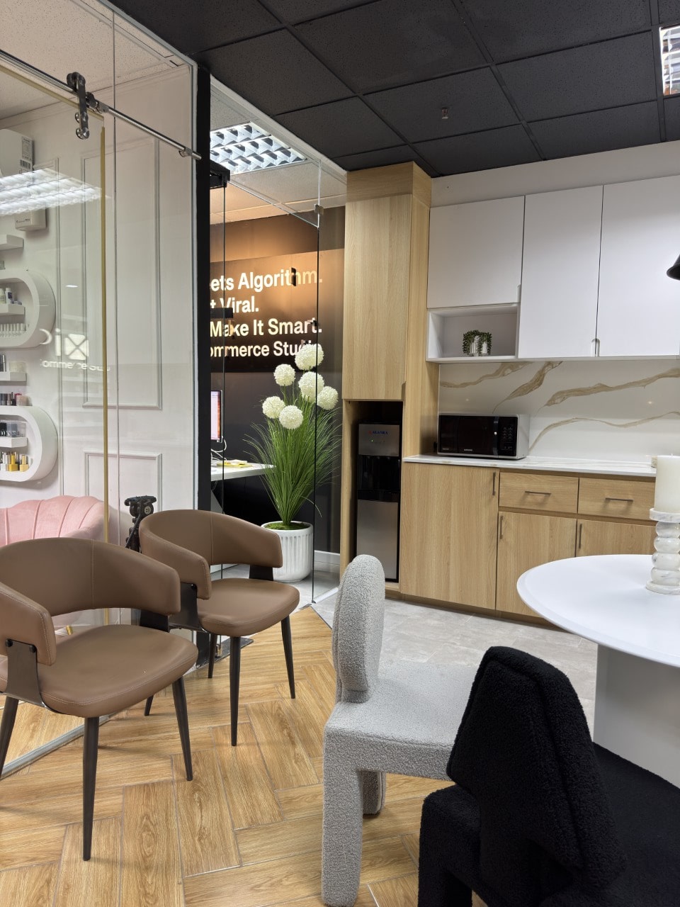 An office breakroom area featuring a kitchenette with wood and white cabinets, brown leather chairs, and a white table.