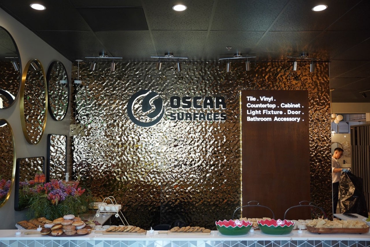 The reception area featuring a textured bronze wall with the Oscar Surfaces logo and a counter with pastries and fruit for an event.