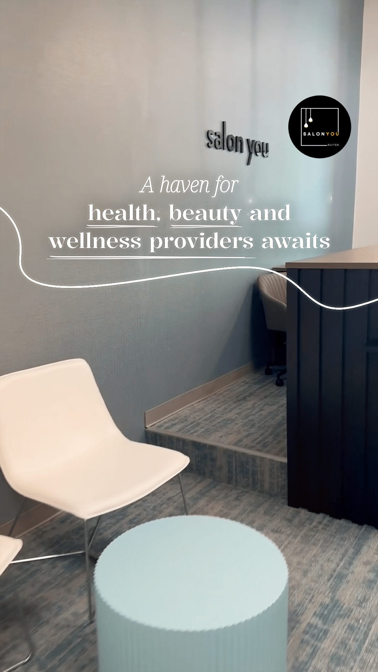 The modern reception area of Salon You Suites with a white chair and light blue table, featuring the text "A haven for health, beauty and wellness providers awaits."