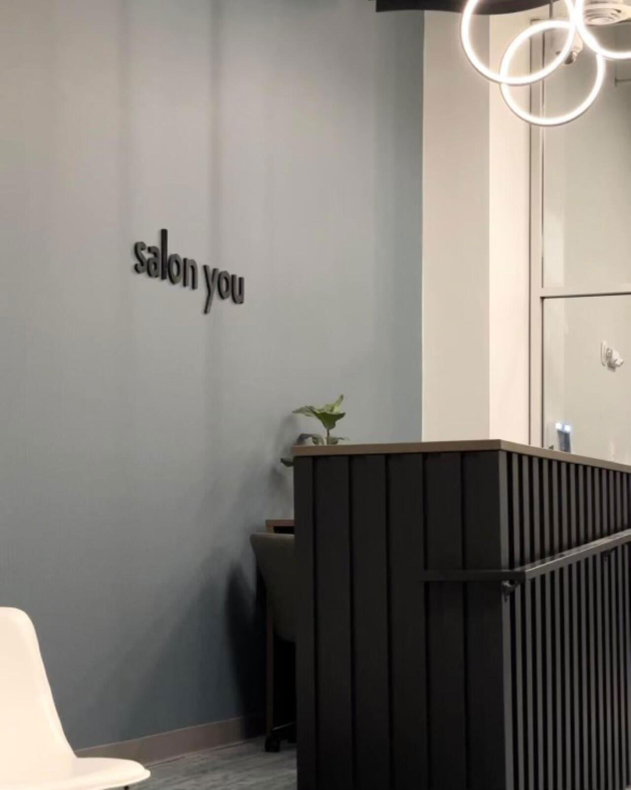 The reception desk area of Salon You with the salon's name in black lettering on a blue-gray wall.