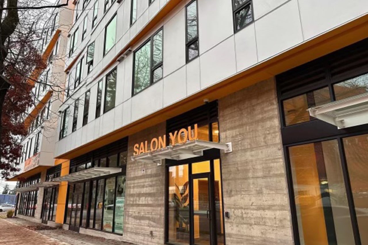 The modern exterior of the Salon You building, showing the entrance with an illuminated sign on a concrete and white facade with orange accents.