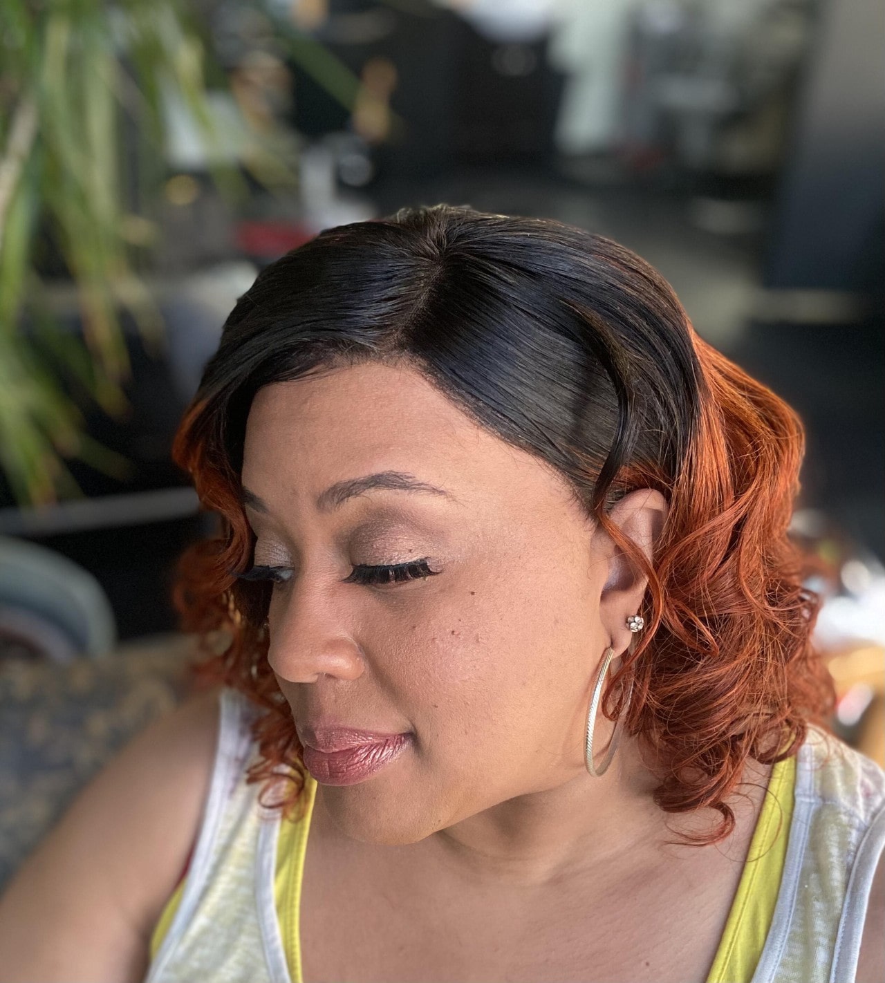 A close-up profile of a woman with a stylish black and auburn ombre hairstyle, looking downwards.