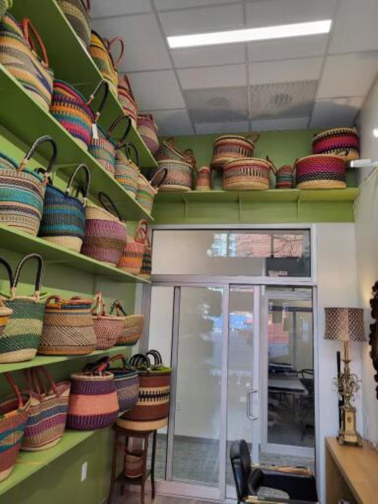 The interior of a retail space with light green walls and shelves displaying a large collection of colorful, hand-woven African baskets and totes.