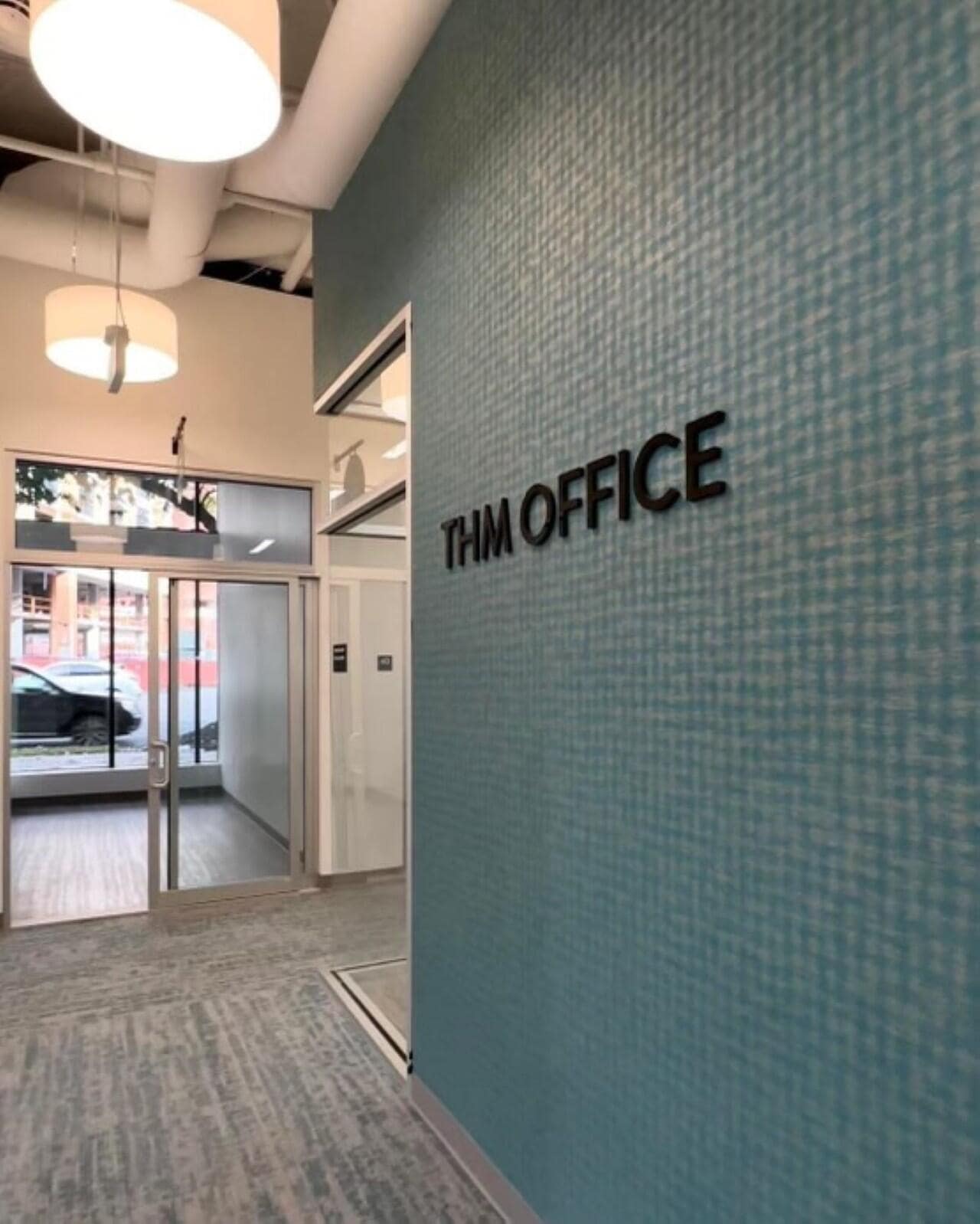 The interior lobby of THM Office featuring a textured blue feature wall with 'THM OFFICE' in black lettering.
