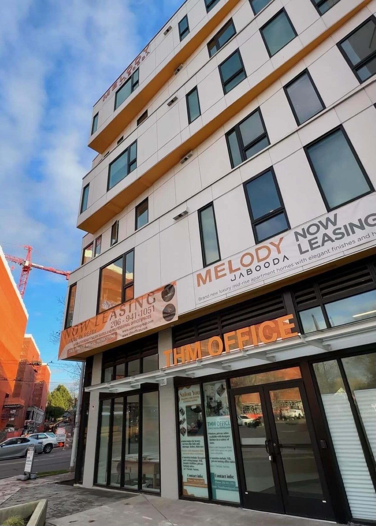  Street-level view of the THM Office and Melody Jabooda apartment building, with large 'NOW LEASING' banners displayed on the facade.