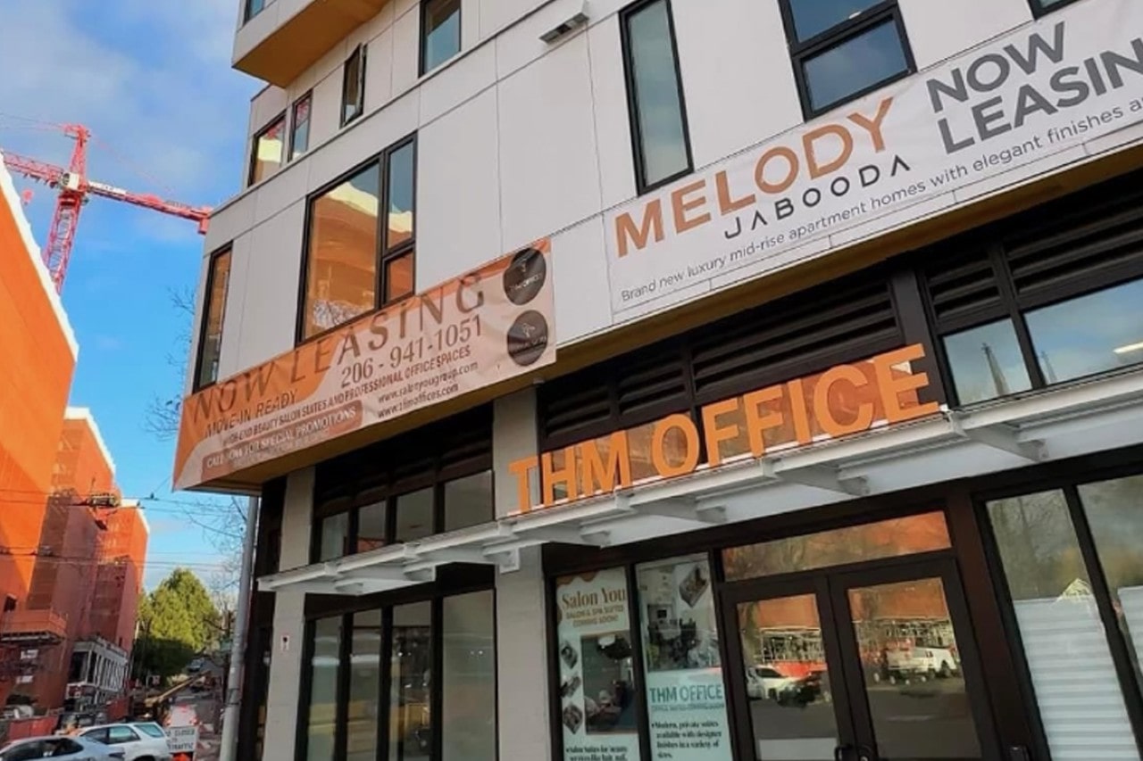 Street-level view of the THM Office and Melody Jabooda apartment building, with large 'NOW LEASING' banners displayed on the facade.